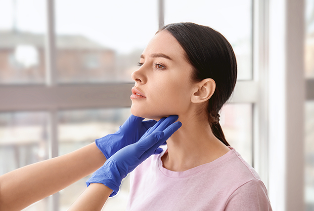 woman gets thyroid gland examined by blue gloved hands touching her throat