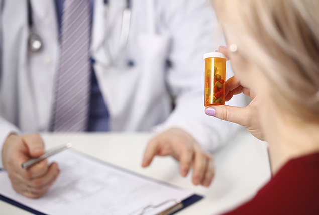woman holds bottle of pills while sitting across from doctor in white coat with clipboard