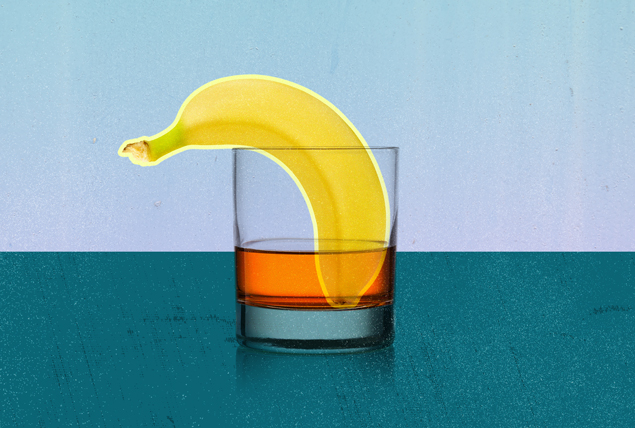 banana in short glass with whiskey on teal table and light blue background
