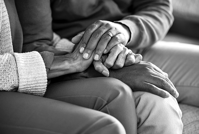 A couple holds hands between their laps.