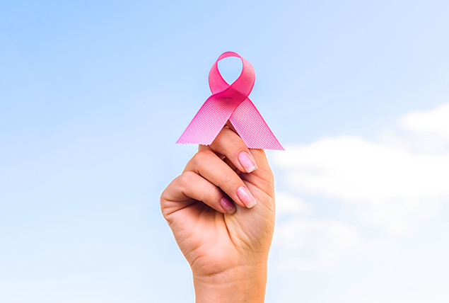 hand holds up finger with pink ribbon wrapped around it on blue sky background