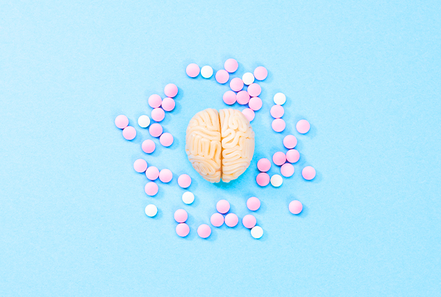 A cluster of pink and white pills surround a human brain on a blue surface.
