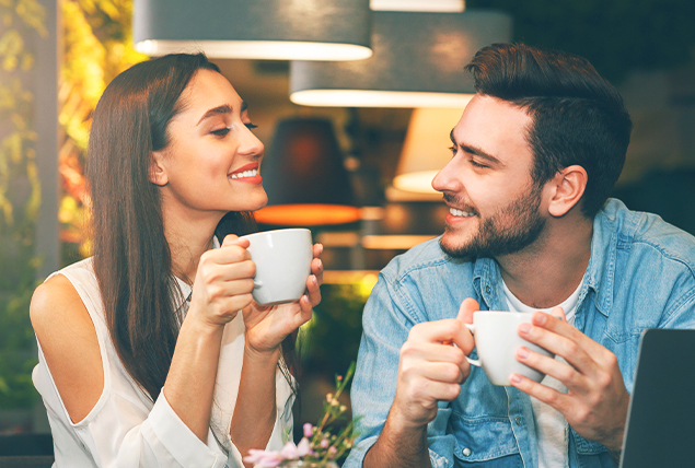 A couple smiles at each other as they have coffee on a date.