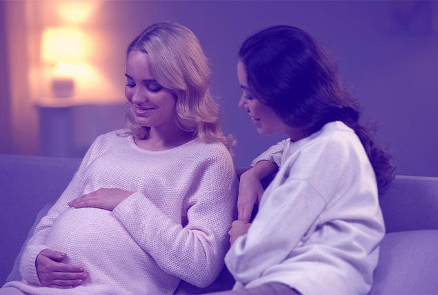 A woman sits next to another who is pregnant as they talk.