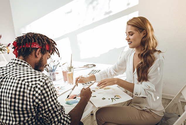 man and woman sit at table and paint watercolors while talking