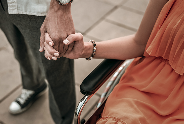 A woman in a wheelchair holds hands with a man standing by her side.