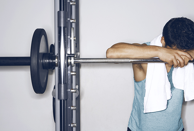 man leans over weight squat bench with towel around his neck