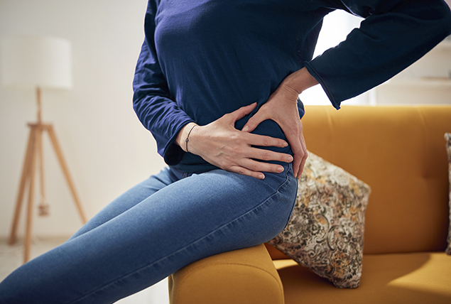 woman sits on side orange couch and grabs her hip in pain