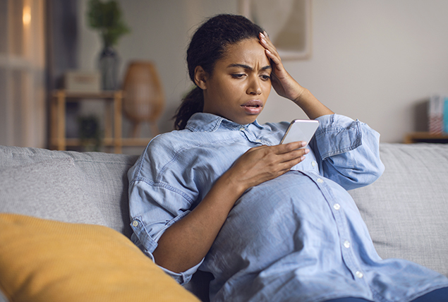 A pregnant woman holds her head in shock as she looks at her cellphone.