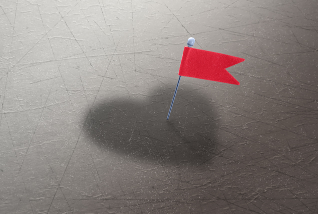 A red flag is pinned in a grey shadow cast on a light grey surface.