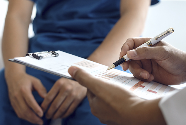 patient in doctors office stand in front of doctor holding a clipboard and pen