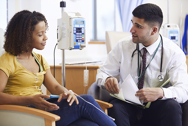 woman sits and talks with doctor in white coat and holding clipboard