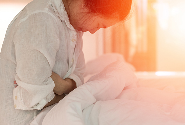 A woman leans over holding her stomach in pain.