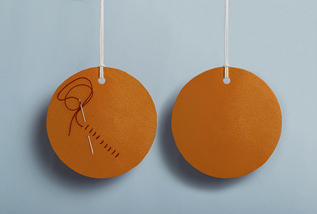 two orange fabric circles hanging from strings, one circle has a needle and thread with stitches