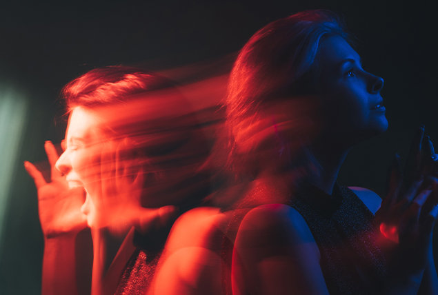 A woman looks to the right under a blue light as an orange shadow of herself screams to the left.