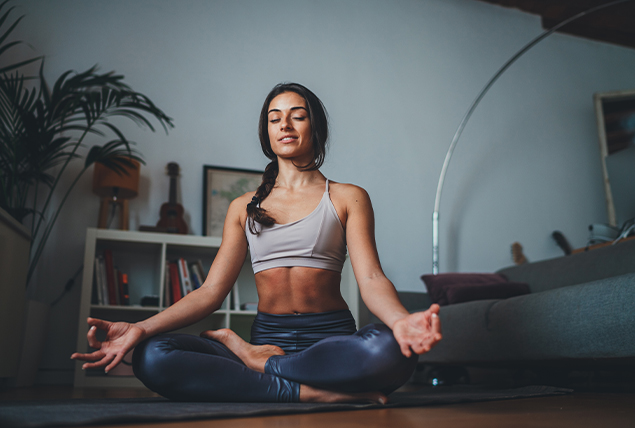 A woman does yoga on the floor in front of her couch.