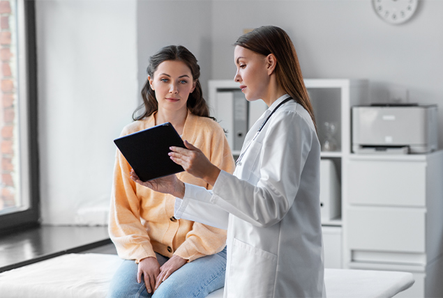 A doctor shows a woman a tablet with medical information on it.