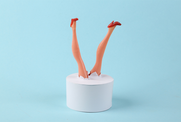 female plastic doll legs with red high heels sticking out of white cylinder on light blue background