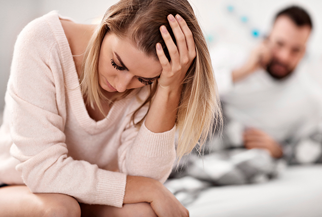 woman holds head bent over in pain as man behind her looks concerned