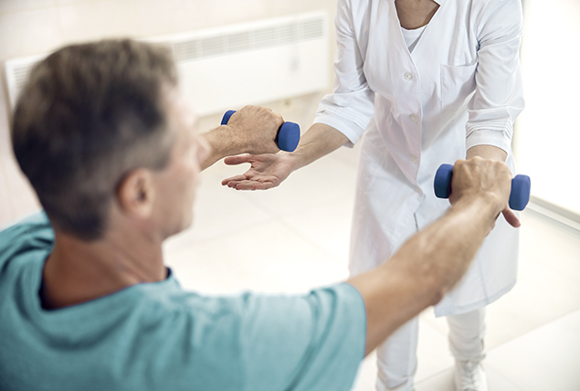 older man lifts blue hand weights with doctor in white coat helping him lift them