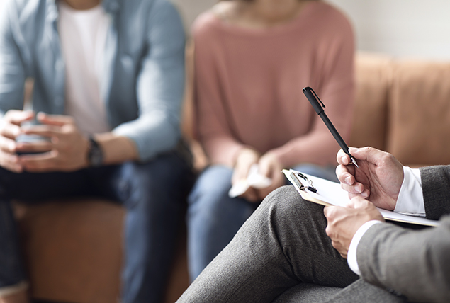 A couple sits together on a sofa in front of a therapist.