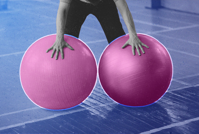 grayscale man holding two pink yoga balls in gray gym