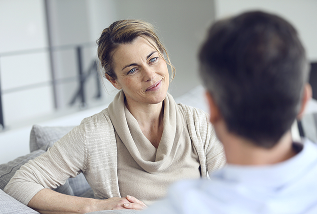 older woman in gray cardigan sits and talks with man in blue collared shirt