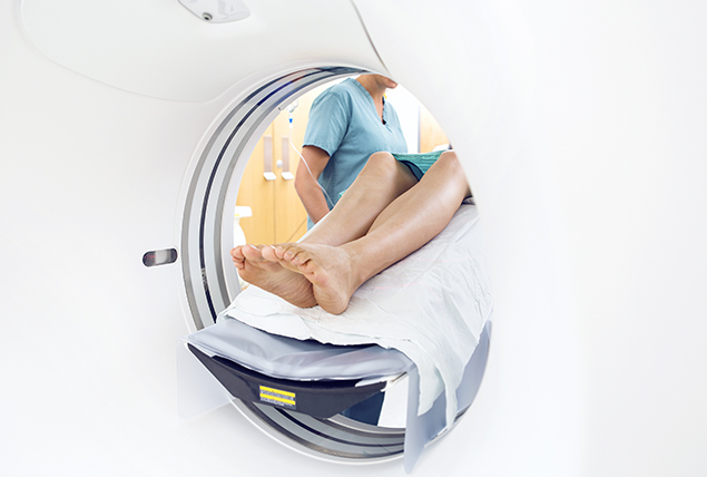 legs sticking out of white MRI machine with nurse in blue scrubs next to patient