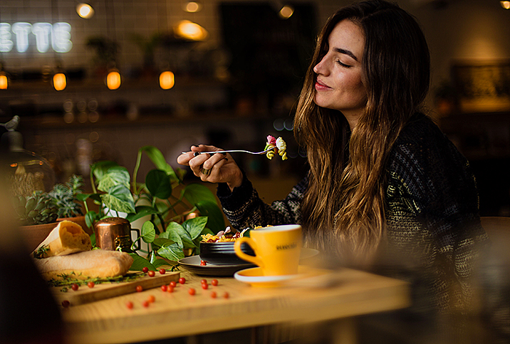 woman sits in darkened restaurant and smiles to herself as she eats pasta