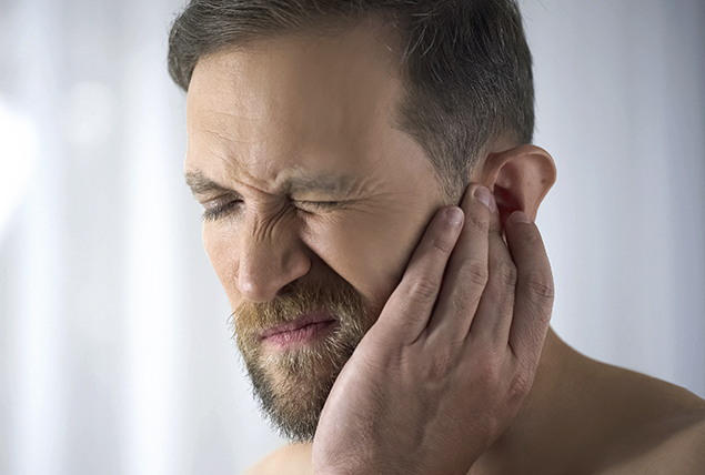 man makes a face in pain and touches his left ear