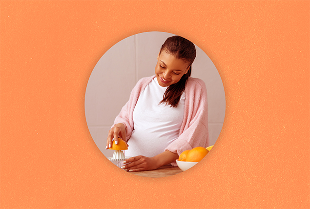 A pregnant woman smiles as she looks down at her hands squeezing juice from an orange.