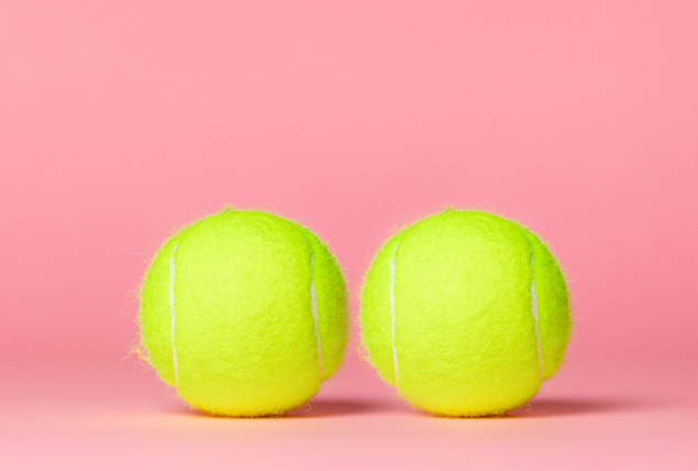 Two tennis balls sit against a pink background.