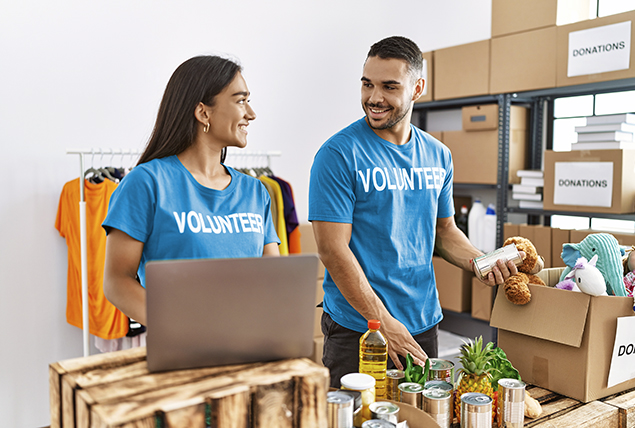A man and a woman sort items in boxes while wearing blue volunteer shirts.
