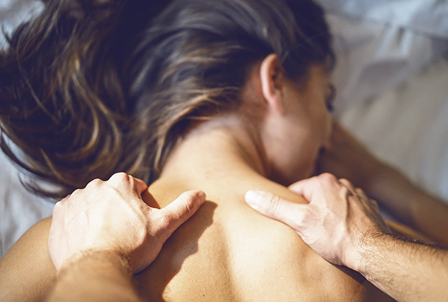 A woman lays on a bed while getting a massage in her shoulders.
