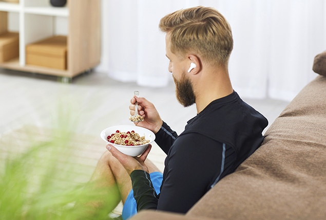 man sits on couch wearing headphone eating bran cereal