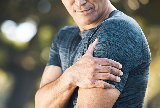 A man holds his upper left arm with his right hand in pain.