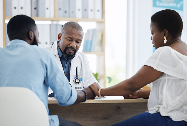 A man and woman sit at a desk talking to a doctor.