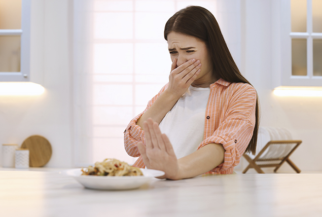A woman pushes a plate of food away as her hand covers her mouth.