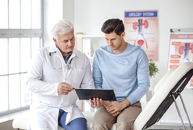 A younger man sits with a doctor looking at an ipad.