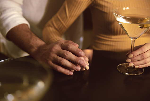 A woman holds a martini glass in one hand as a man holds her other hand.
