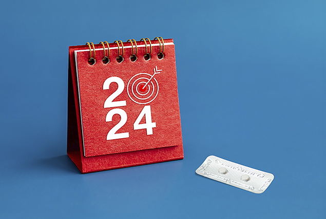 A packet of pills sits next to a red calendar page that says 2024 with a bullseye in place of the zero.