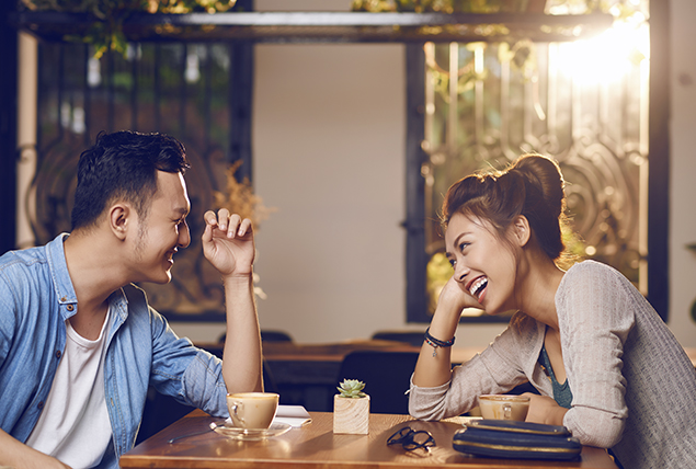 A man and woman sit across a table laughing while on a date.