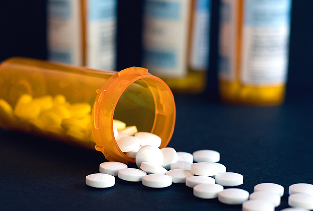 One bottle of white pills is tipped over in front of three other prescription bottles.