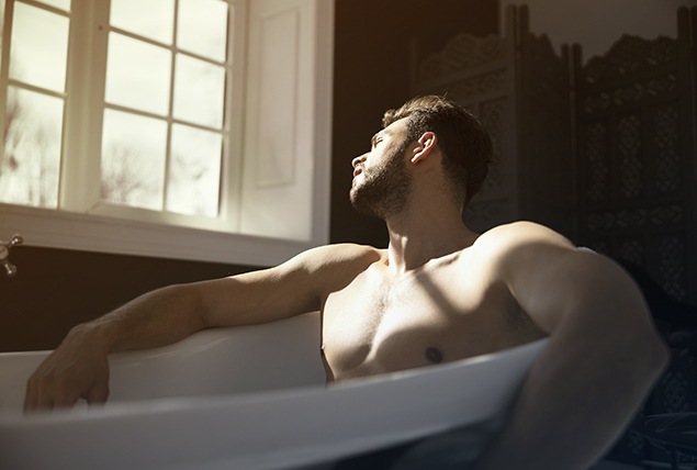 A man sits in a bathtub looking out a window towards the sun.
