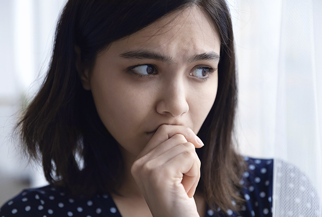 An anxious woman holds her hand to her chin as she looks to the side.