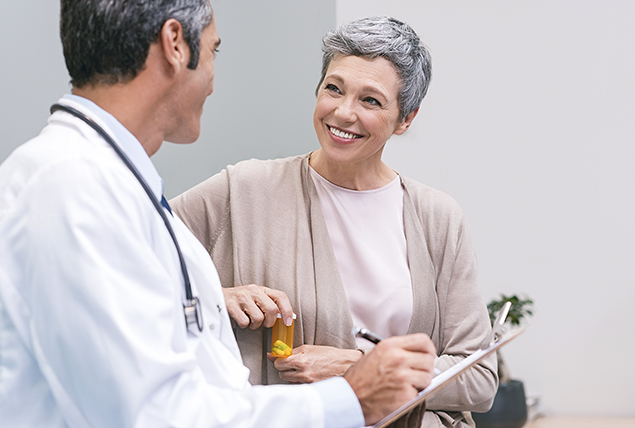 A woman going through menopause holds a pill bottle while talking to a doctor.