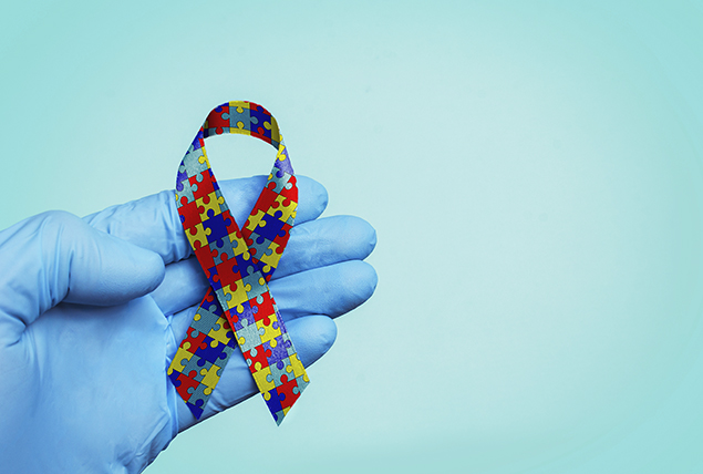 A blue-gloved hand holds a ribbon made up of puzzle pieces in multiple colors.