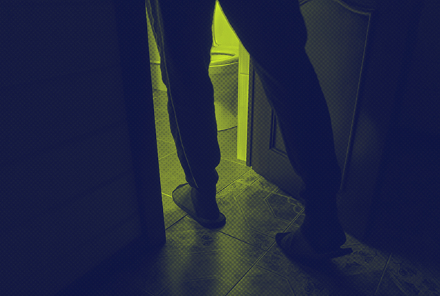 A pair of legs walk into a dimly lit bathroom at night.