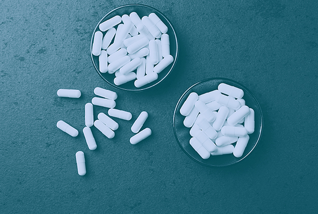 Two circular trays hold white pills with a few scattered onto a teal surface.