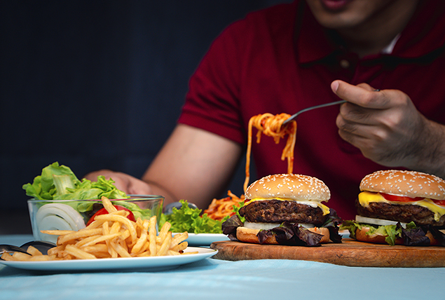 A person sits in front of a table with two cheeseburgers and fries on it.